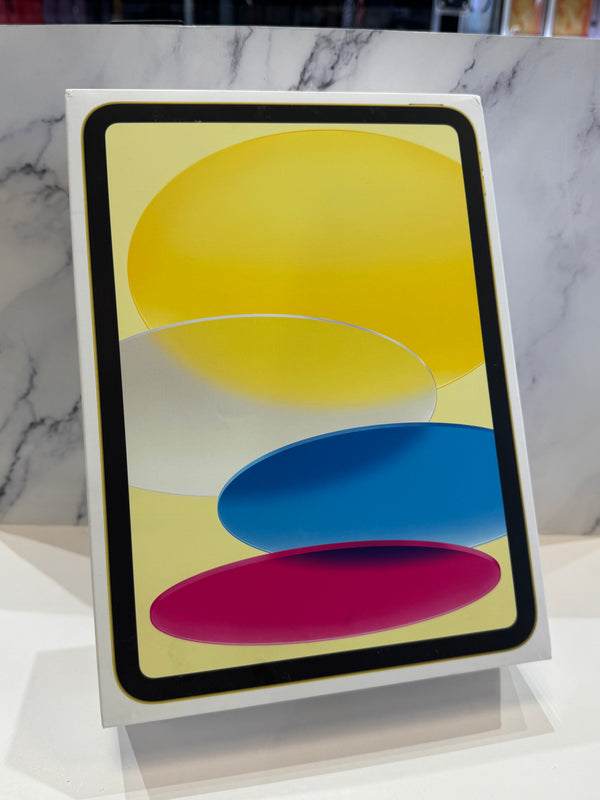 A tablet device in a white retail box, shown standing upright on a display stand against a white marble-patterned background. The screen displays an abstract design with overlapping yellow, blue, pink, and white shapes.