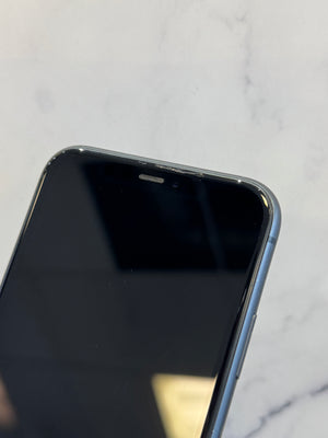 Close-up of the top-left corner of a smartphone with a black screen and a blue-gray metallic edge, resting on a light marble surface.