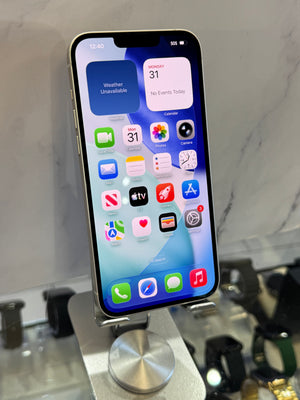 A silver Apple iPhone with a black front display resting on a metallic stand in a retail setting, with blurred watches and a marble-patterned background.