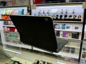 A black tablet in a protective folio case with an attached keyboard, photographed inside a retail store with display shelves in the blurred background.