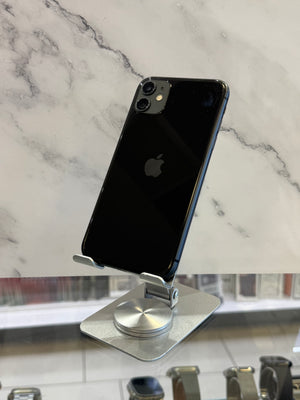 A black Apple iPhone with a glossy finish, shown from the back, resting on a silver magnetic display stand over a white marble-patterned surface.