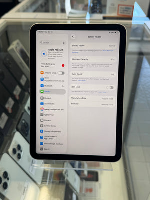 An Apple iPad showing the Battery Health settings screen on its screen, displayed on a clear stand in a retail or service environment.