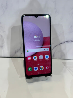 A black smartphone with a front-facing notch display stands upright on a small metal display stand against a white marble-patterned background.