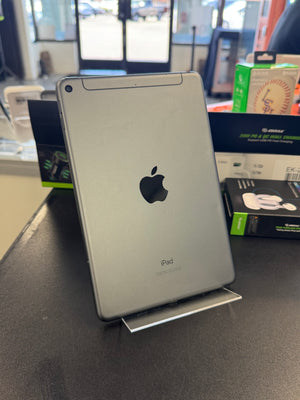 A silver Apple iPad tablet standing upright on a metal display stand on a dark tabletop, with product packaging boxes visible in a store or office setting in the background.