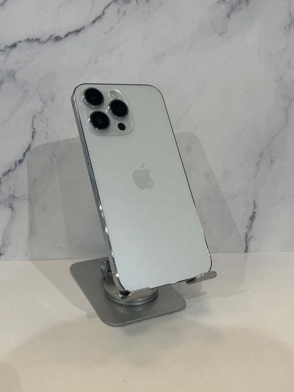 A silver Apple iPhone 12 Pro shown from the back, resting on a clear stand against a white marble-patterned background.