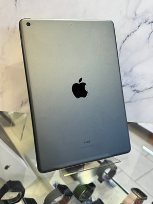 A silver Apple iPad shown from the back, standing on a clear display stand in front of a marble-patterned background.