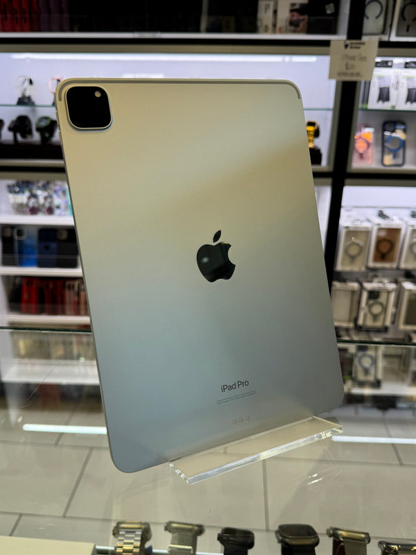 A silver Apple iPad Pro tablet standing upright on a clear display stand inside a retail store, with the Apple logo and 'iPad Pro' text visible on the back.