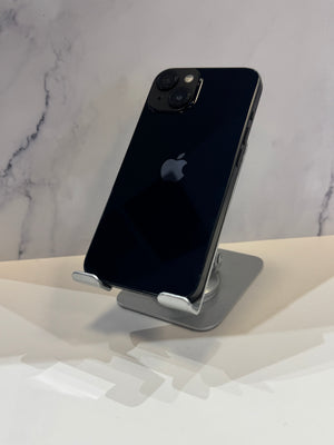 A black Apple iPhone mounted on a silver wall-mounted phone stand, shown against a white marble-patterned wall and a white wall corner.