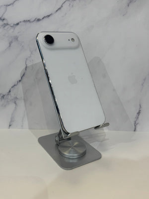 A silver Apple iPhone with a white back is displayed on a metallic silver stand against a white marble-patterned background.
