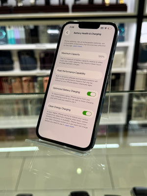 Smartphone displaying battery health settings on a clear stand with a blurred store background