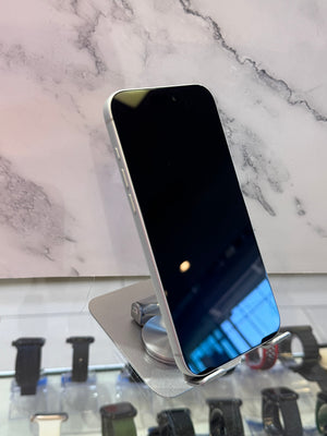 A silver smartphone with a black screen stands upright on a small metallic display stand. The phone is photographed in a retail-like setting with a marble-patterned backdrop and watch displays visible below.