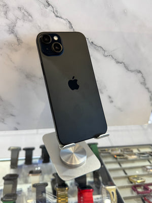 A black Apple iPhone 12 Pro shown from the back, resting on a silver metal display stand in front of a white marble-patterned background.