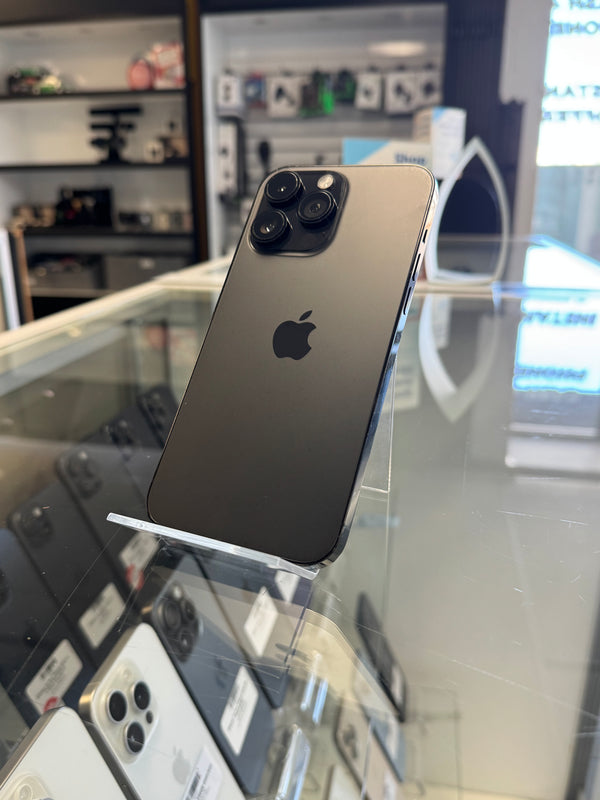 A black Apple iPhone Pro showing its back panel with the triple-camera array and Apple logo, displayed on a clear stand inside a retail store.