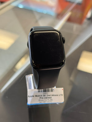Black Apple Watch SE 2nd Gen LTE with a black band, resting on a reflective dark surface next to its retail price tag.
