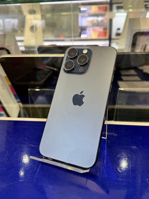 A silver Apple iPhone 12 Pro shown from the back, resting on a clear display stand against a blue and glass retail display background.