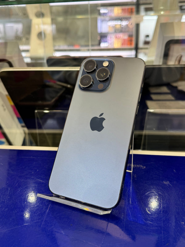 A silver Apple iPhone 12 Pro shown from the back, resting on a clear display stand against a blue and glass retail display background.