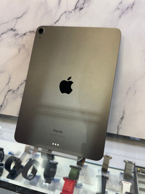 An Apple iPad Air shown from the back, featuring a dark metallic gray finish with the black Apple logo in the center, resting on a white marble-patterned surface.