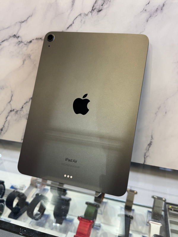 An Apple iPad Air shown from the back, featuring a dark metallic gray finish with the black Apple logo in the center, resting on a white marble-patterned surface.
