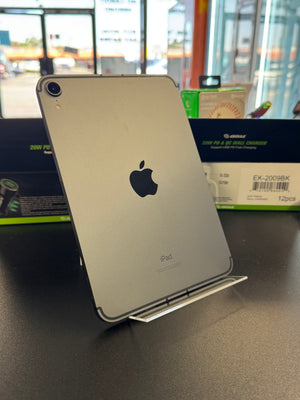 A silver Apple iPad standing upright on a metal display stand on a dark tabletop, with retail packaging boxes visible in a store setting behind it.