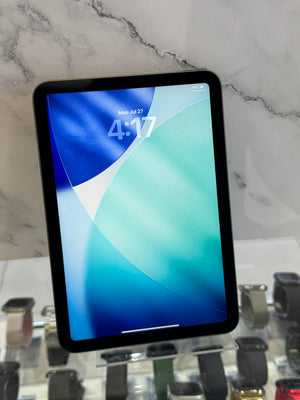 A black tablet with a blue and green lock screen wallpaper, resting on a white marble-patterned surface next to a display of smartwatches.