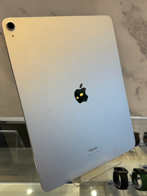 A silver Apple iPad Air shown from the back, standing on a clear display stand in a store setting with a marble-patterned wall behind it.