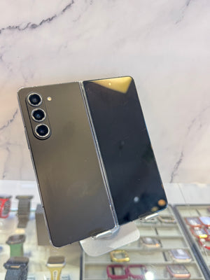 A dark gray Samsung Galaxy S24 Ultra foldable smartphone shown open, with the back panel on the left and the front display panel on the right, resting on a display stand in a retail setting.