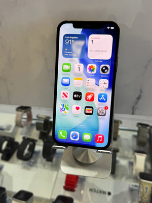 A black iPhone with its screen turned on, displayed on a silver stand in a retail setting with watch displays blurred in the background.