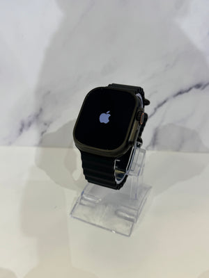 A black Apple Watch with a black band displayed on a clear acrylic stand against a white marble-patterned background.