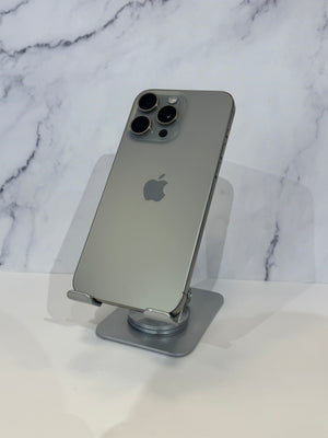 A silver Apple iPhone 12 Pro shown from the back, resting on a small metallic stand against a white marble-patterned background.
