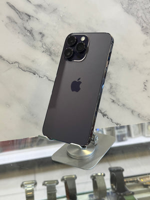 A dark gray Apple iPhone Pro shown from the back, resting on a silver display stand over a white and gray marble surface.