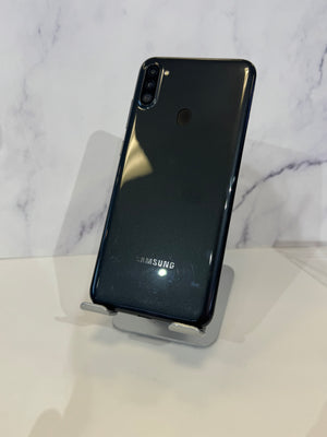 A Samsung smartphone shown from the back, resting on a small display stand against a light marble-patterned background.