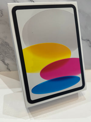 A white Apple iPad in its original retail box, standing upright on a white surface against a light gray marble-patterned background.
