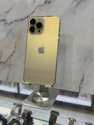 A gold-colored Apple iPhone Pro Max standing upright on a silver display stand, set against a white marble-patterned background.