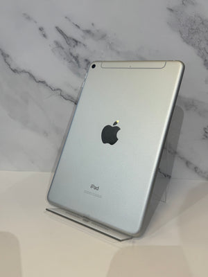 A silver Apple iPad shown from the back, standing upright on a clear acrylic display stand against a white marble-patterned background.