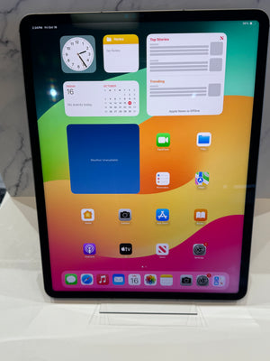 An Apple iPad with the display on showing multiple colors and app icons.  Device is standing upright on an acrylic stand. 