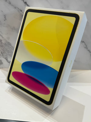 A white Apple iPad box standing upright on a white surface, with an image of a tablet screen and displaying a colorful abstract wallpaper. The background is a light gray marble-patterned wall.