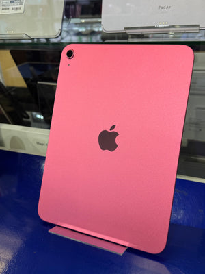 A pink Apple iPad shown from the back, featuring the black Apple logo in the center and a kickstand on the right side, photographed in a retail display setting.