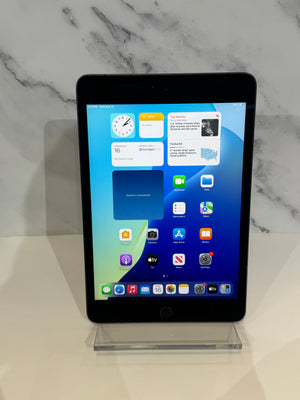 An Apple iPad with a black bezel and a colorful home screen, displayed on a clear acrylic stand against a white marble-patterned background.