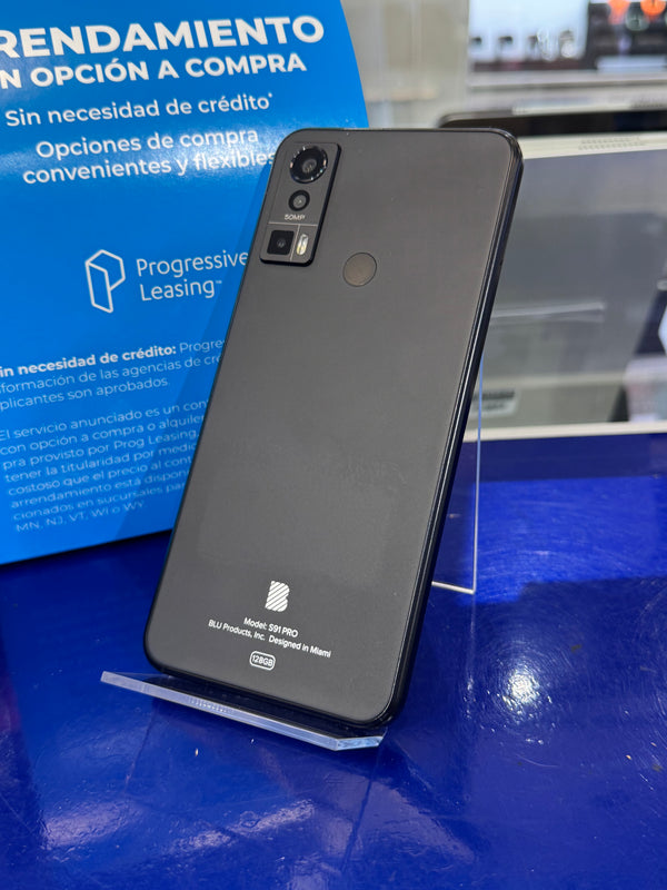 A black Google Pixel Pro smartphone standing upright on a clear display stand on a blue table, with a blue leasing sign in the background.