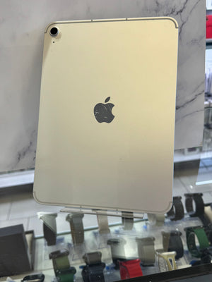 A silver-colored Apple iPad shown from the back, resting on a display stand in a retail or showroom setting with marble walls and other devices visible in the background.