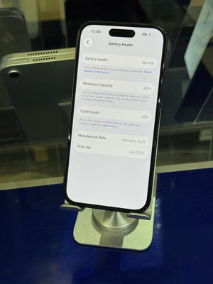 A black smartphone displayed in a silver stand, showing the battery health settings screen on its white home screen. The phone is photographed on a reflective blue surface.