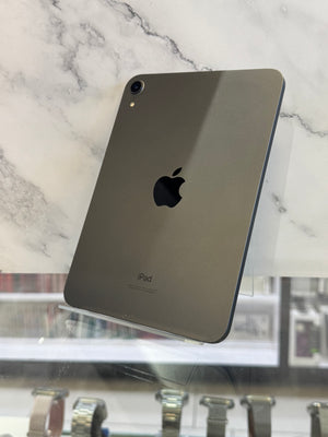A dark gray Apple iPad shown from the back, resting on a white marble-patterned surface with a blurred store background visible on the right.