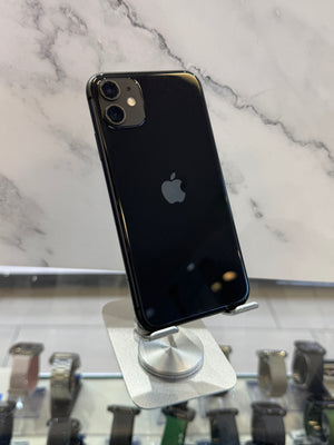A black Apple iPhone with a glossy back is shown from the rear, resting on a white magnetic display stand on a white marble-patterned surface.