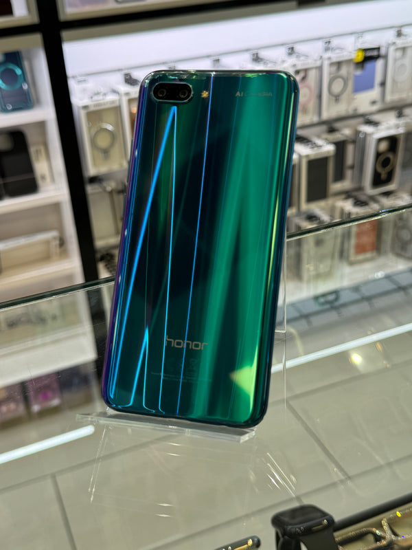 A green and blue iridescent Honor smartphone with a metallic finish, standing on a clear display stand inside what appears to be a retail store.