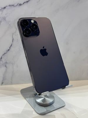 A dark blue-gray Apple iPhone 13 Pro shown from the back, resting on a silver metal stand against a white marble-patterned background.