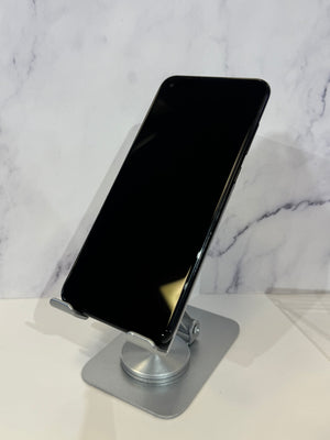 A black smartphone displayed at an angle on a silver metal stand, set against a white marble-patterned background.