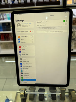 An iPad displaying the Settings app, showing the battery percentage and connection options, photographed in a retail or showroom environment with a glass display stand below.