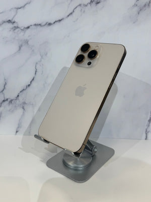 An Apple iPhone in light gold is shown from the back, resting on a silver metal stand against a white marble-patterned background.