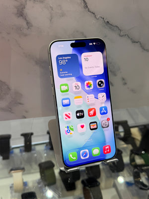 A silver Apple iPhone with its screen turned on, displaying the home screen, resting on a clear display stand in a retail setting.