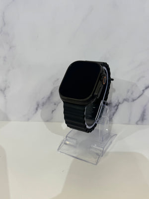 A black smartwatch with a black ribbed band is displayed on a clear acrylic stand against a white marble-patterned background.